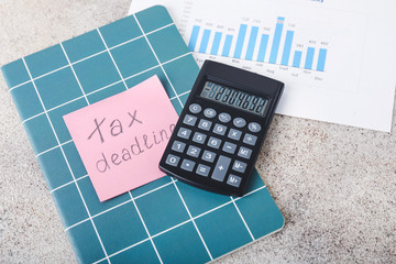 Calculator, notebook and paper with text TAX TIME on table
