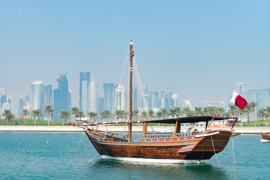 Retro historical boat with blurred panoramic view of modern skyline of Doha and green palms on background