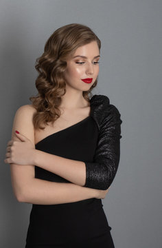 emotional portrait of a girl with blond wavy hair in vintage style. Young girl in a black dress and with red lipstick on a gray background