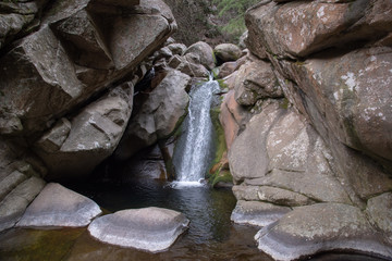 Wide view of a little waterfall in the middle of massive rocks