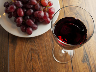Fresh red grapes on a white plate and a glass of a red wine on a wooden table.