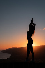 Silhouette of woman enjoying freedom feeling happy at sunset with mountains and sea on background
