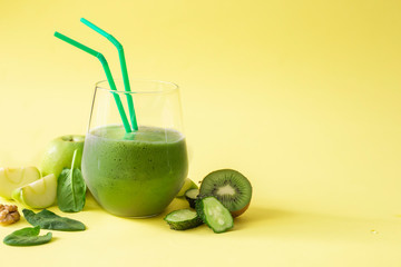 Dietary healthy green smoothie from cucumber, spinach, green apple and kiwi on a yellow background. Image with horizontal orientation and copy space.