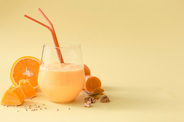 Dietary healthy vegetarian smoothie made of pumpkin, carrot, orange, nuts and green sprouted buckwheat in a glass glass on a yellow background.