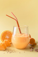 Dietary healthy vegetarian smoothie made of pumpkin, carrot, orange, nuts and green sprouted buckwheat in a glass glass on a yellow background.