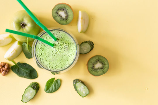Dietary healthy green smoothie from cucumber, spinach, green apple and kiwi on a yellow background. Image with horizontal orientation and copy space. View from above
