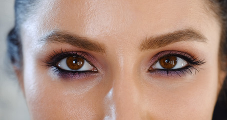 Close-up of eyes of young woman looking playfully smiling straight and to the sides at camera after applying professional makeup. Eyes of the models are beautifully executed with shadows, eyelashes