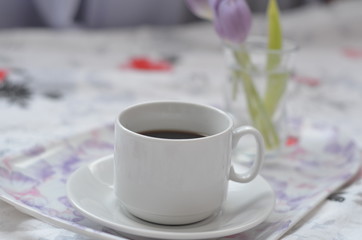 a cup of coffee tray with spring flowers on pink bedding. Relaxing, or working, or writing diary or blog in bed at home. with tablet