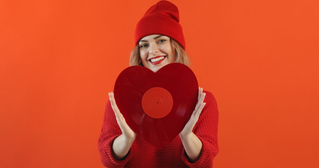Valentine's Day portrait cheerful girl holding red vinyl record shape of heart on red background. Symbol of love. Holiday all lovers. Feelings, emotions woman. Music. Monotone. Copy space. Lifestyle
