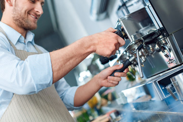 Coffee Passion. Young barista at coffee shop inserting portafilter into espresso machine close-up smiling cheerful