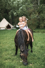 Horseback, two children girls, sisters, riding a horse outdoors, smiling and hugging each other....