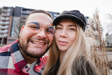 Fototapeta premium Two lovers making funny selfie, Portrait of cheerful laughing funny young people. Cute couple of hipsters is walking in spring park. Emotion facial expression. Beautiful sunny day.