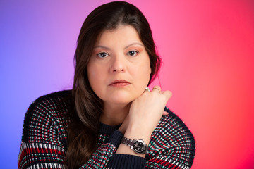 Lady closeup studio portrait over blue and red gradient background made with gel on flashlights. She is caucasian with long hair. She is serious and looking at the camera. One hand is on her face.