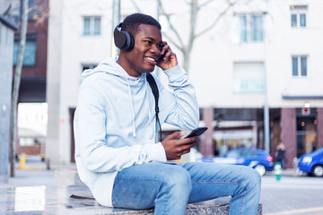 Young Black man sitting on bench while listening music by headphones