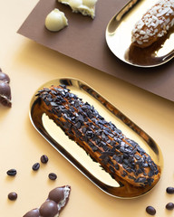 Eclairs on gold plates on a paper background in the style of minimalism.
