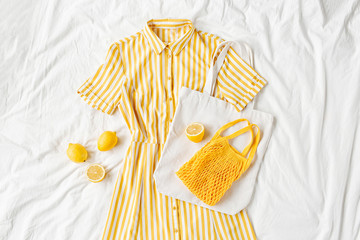 Yellow dress with stripes with eco bag and lemons on white bed. Women's stylish  summer outfit. Trendy clothes. Flat lay, top view.