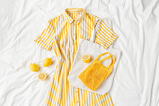 Yellow dress with stripes with eco bag and lemons on white bed. Women's stylish  summer outfit. Trendy clothes. Flat lay, top view.