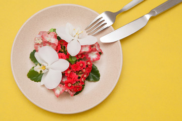Plate with flowers on a yellow background. Copy space. Diet, proper nutrition concept.
