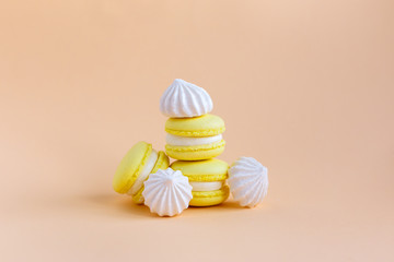Yellow macarons and white marshmallows on a peach pastel background.