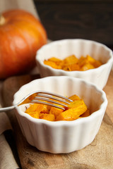 Piece of pumpkin on steel fork , baked pumpkin in white ceramic bowl on wooden background