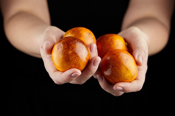 Unpeeled blood orange friuts in hands on black background