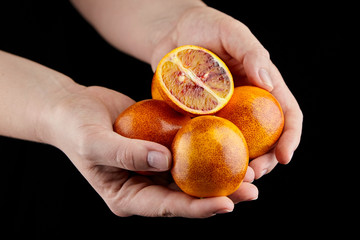 Red or blood orange fruits in hands on black background