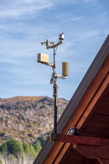 Meteorological station placed on a wooden roof. At the back, a mountain with foliage and a semi...