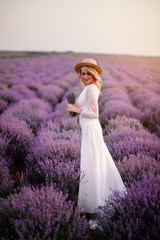 Young woman in white dress walks through blooming lavender field at sunrise