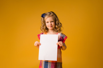 baby girl holding white sheet.Cute little girl with white sheet of paper.yellow background.copy spase.Little girl holding empty sheet of a paper