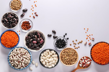 Red and brown lentils, black, brown and white beans are legumes that contain a lot of protein are located in bowls on white background, concept is healthy eating