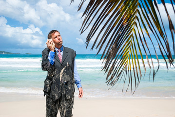 Stranded castaway businessman standing on the beach in his ragged suit, having an imaginary conversation on his shell phone