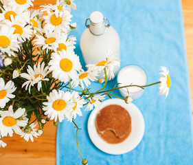 Simply stylish wooden kitchen with bottle of milk and glass on table, summer flowers camomile, healthy foog moring concept