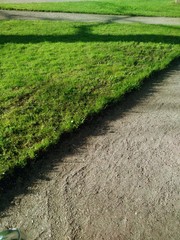 The edge of the green lawn along the dirt path in the park. goes into perspective