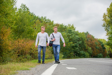 Obraz premium Guys hitchhiking on road. Tourist traveler travel auto stop. Transporting issues. Men backpack walking road. Twins walk along road. Brothers friends nature background. Long way. Adventure concept