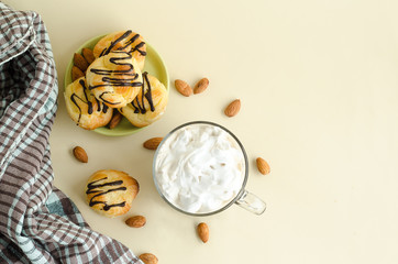 top view of custard pastries profiteroles. small eclairs with chocolate icingб cappuccino coffee drink with lush foam and whipped cream on yellow background with copy space