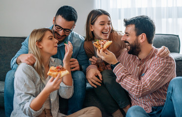 Group of cheerful friends eating delicious pizza at home