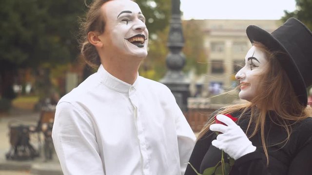 Two happy mime on a date on the street near the clock. Happy man giving a flower to his girlfriend