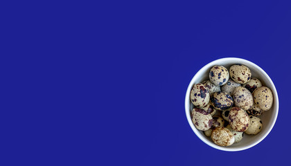 Quail eggs in a white bowl on a blue background. Top view. Copy space.