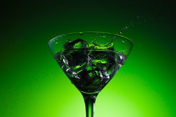 Splash in a Martini glass. Ice cubes in a cocktail glass. Beautiful green emerald background. 
