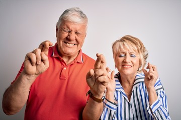 Senior beautiful couple standing together over isolated white background gesturing finger crossed smiling with hope and eyes closed. Luck and superstitious concept.
