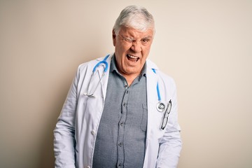 Senior handsome hoary doctor man wearing coat and stethoscope over white background winking looking...