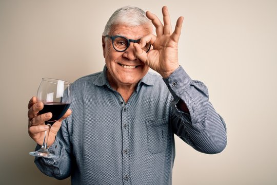 Senior Handsome Hoary Man Drinking Glass Of Red Wine Over Isolated White Background With Happy Face Smiling Doing Ok Sign With Hand On Eye Looking Through Fingers