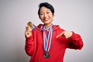 Young beautiful asian girl winner wearing medals over isolated white background with surprise face pointing finger to himself