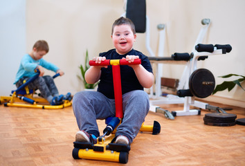 happy young kid with down syndrome exercising on inclusive sport equipment, developing muscular strength at rehabilitation center © Olesia Bilkei