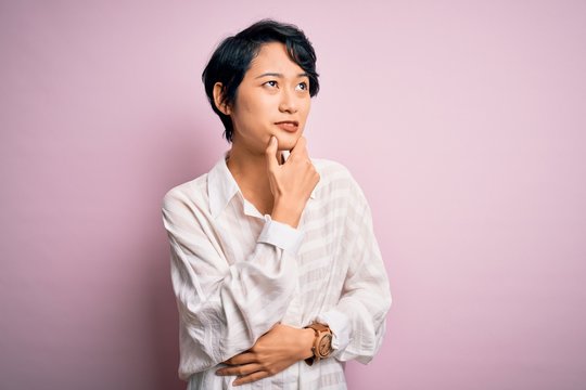 Young beautiful asian girl wearing casual shirt standing over isolated pink background Thinking worried about a question, concerned and nervous with hand on chin