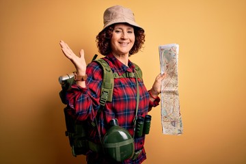 Middle age curly hair hiker woman hiking wearing backpack and water canteen holding city map very happy and excited, winner expression celebrating victory screaming with big smile and raised hands