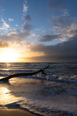 beautiful sunset over the sea, panorama view of a dramatic sunset with dark clouds. rain clouds or storm clouds before the storm, tree trunk lies in the water on the bea