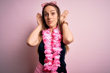 Young beautiful blonde woman wearing swimsuit and floral Hawaiian lei over pink background Doing bunny ears gesture with hands palms looking cynical and skeptical. Easter rabbit concept.