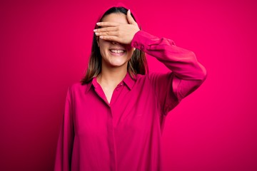 Young beautiful brunette girl wearing casual shirt standing over isolated pink background smiling and laughing with hand on face covering eyes for surprise. Blind concept.