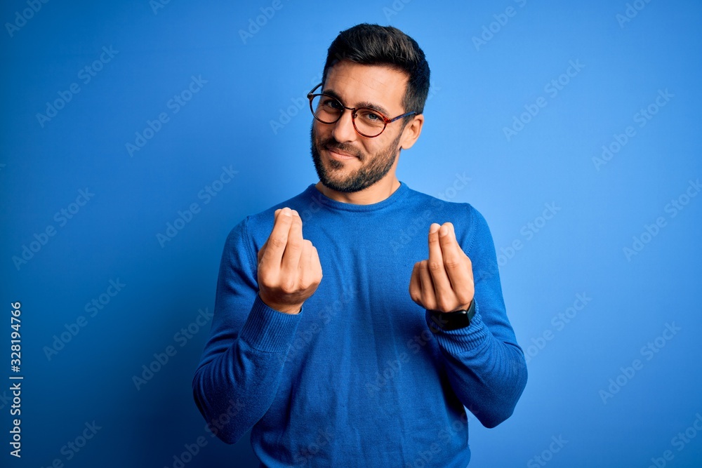 Poster young handsome man with beard wearing casual sweater and glasses over blue background doing money ge